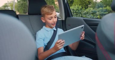 Çekici, pozitif sarışın, 10 yaşında, emniyet kemeriyle arabanın arka koltuğuna bağlanmış, tablet zımbırtıyla oyunlar oynuyor, trafik güvenliği kavramı...