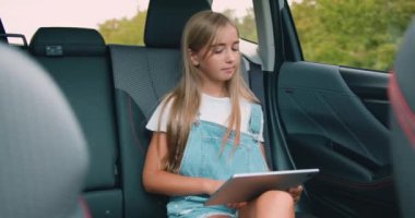 Çekici, mutlu, güler yüzlü, şık elbiseli 12 yaşında bir kız. Arka koltuktaki lüks otomobilde elinde tablet zımbırtıyla oturuyor ve zaman zaman pencereye bakıyor.