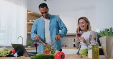 Gülümseyen kadın, modern mutfakta kocasıyla telefonda konuşuyor ve salata pişiriyor. Evde birlikte mutlu bir aile. Yavaş çekim.