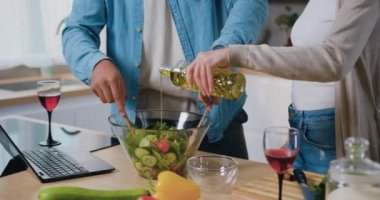 Kapatın. Mutfakta çok ırklı bir çift sebze salatası pişiriyor. Beyaz salata kasesine yavaş çekimde ayçiçeği yağı döken bir kadın. Sağlıklı öğle yemeği. Mutfak ve vejetaryenlik. Yavaş çekim.