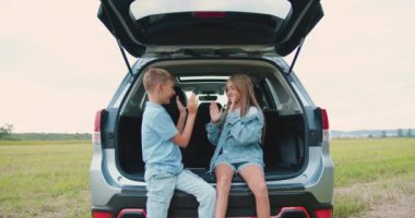 Şirin, neşeli, oyuncu, 10-12 yaşında erkek ve kız kardeş, yeşil çimenlikte duraklarken araba bagajında oyun oynuyorlar. Aile tatili kavramı.