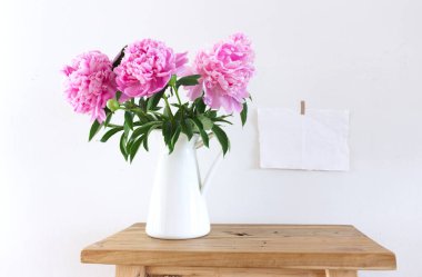 Masaüstü sahnesi. Eski ahşap bir bankta, masa arkasında, beyaz vazoda pembe şakayık çiçekleri. Mesajı iletmek için kopyalama alanı ile birlikte. Bahar çiçekleri. Bahar arkaplanı.