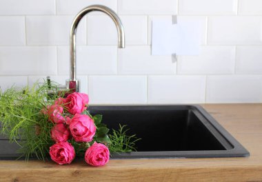 Mutfağın içini kapatıyoruz. Beyaz tuğla duvar, metro fayansları, ahşap tezgah. Siyah lavaboda bir buket pembe gül. Modern İskandinav tasarımı, ev dekorasyonu, temizlik konsepti.