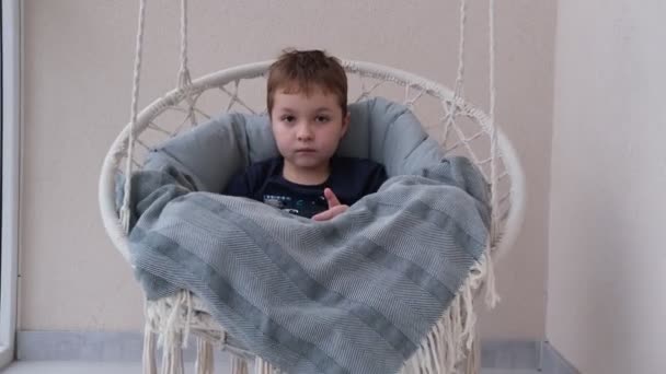 Um menino pequeno com um telefone em suas mãos está montando um balanço — Vídeo de Stock