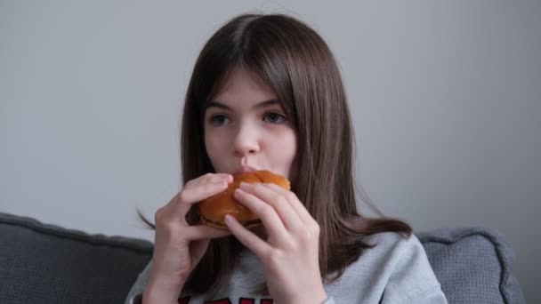 Девочка, подросток ест бургер дома на диване. нездоровое питание, концепция быстрого питания — стоковое видео