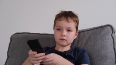 Küçük bir çocuk elinde uzaktan kumanda tutuyor, programları değiştiriyor, TV 'de oyunlar oynuyor.