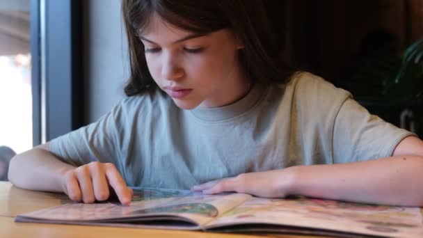 Pequena, jovem adolescente lê o menu em um café — Vídeo de Stock