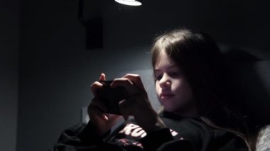 Küçük bir kız çizgi film izler, gece karanlıkta akıllı telefondan oyunlar oynar.