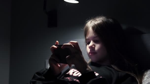 Uma menina assiste desenhos animados, joga jogos em um smartphone à noite, no escuro — Vídeo de Stock