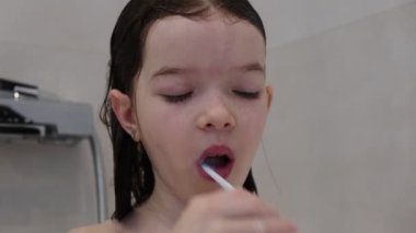 Küçük kız banyoda dişlerini fırçalıyor.