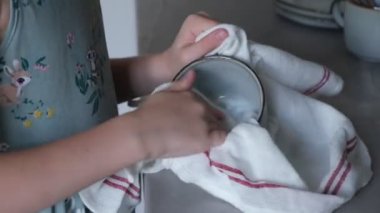 Küçük kız bardakları havluyla siler, annesine mutfakta yardım eder.