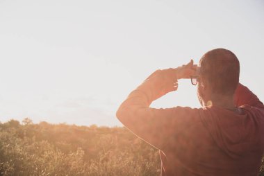 Bir adam yüksek çimlerde dikiliyor ve uzaklığa bakıyor. Gözleri parlak günbatımı güneşinden koruyor. keşif kavramı