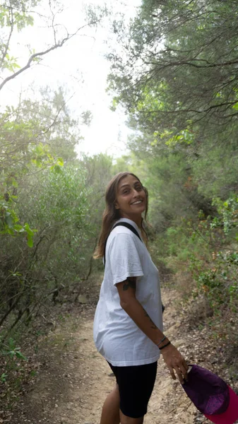 young latina woman tattooed smiling and walking in the forest with cap in hand. autumn concept.vertical.strong of itself. wearing white shirt