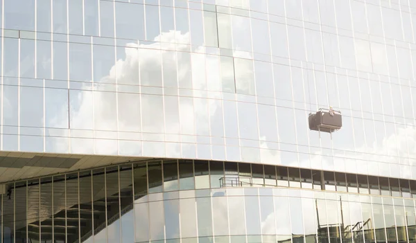 Worker cleaning glass curtain wall at high rise building with rope. Special Job concept.horizontal. with clouds glittering on the glass