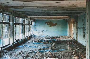 Kirli, kırık camlı terk edilmiş bir bina, yakın çekim manzarası, boyanın ve alçının soyulması, yerde inşaat atıkları.