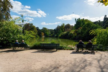 Paris, Fransa - Ekim 06 2022: Parisliler güneşli bir sonbaharın ilk günlerinde Parc Montsouris gölünün kıyısında güneşleniyorlar