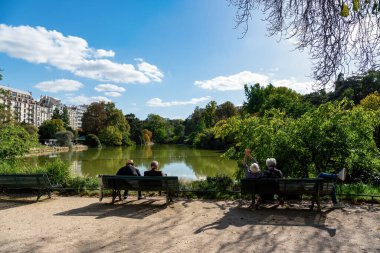 Paris, Fransa - Ekim 06 2022: Parisliler güneşli bir sonbaharın ilk günlerinde Parc Montsouris gölünün kıyısında güneşleniyorlar