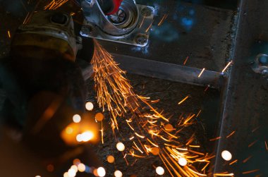 Açı öğütücü kullanan sanayi işçisi metali kesiyor. Açı öğütücüyle çalışan ve turuncu kıvılcımları olan bir işçi. Kesme ve öğütme çeliği için alet. Endüstriyel işyerinde güvenlik. Metal fabrikası endüstrisi.