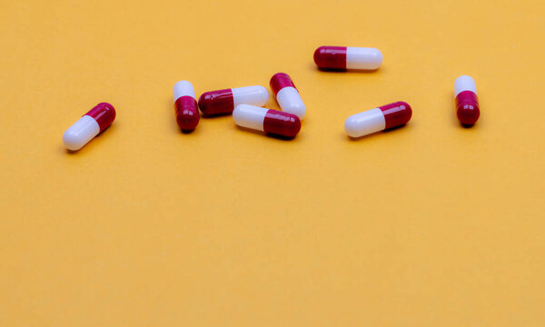 Antibiotic capsule pills on yellow background. Pharmaceutical industry. Prescription drug. Red-white capsule pills. Pharmaceutical product. Pharmacy web banner. Health insurance and health budget.