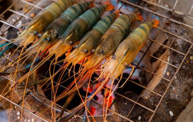 Kömür ızgarasında ızgara karides. Dev tatlı su karidesleri yanan kömür ateşinde ızgara yapıyor. Barbekü ızgarasında pişen dev nehir karidesi. Parti için yemek pişiriyorum. Tayland yemek kültürü.