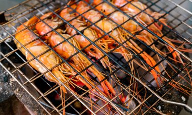 Kömür ızgarasında ızgara karides. Dev tatlı su karidesleri yanan kömür ateşinde ızgara yapıyor. Barbekü ızgarasında pişen dev nehir karidesi. Parti için yemek pişiriyorum. Tayland yemek kültürü.