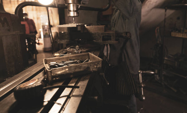 Tools in plastic box on blur milling machine and worker in workshop. Worker working with milling machine. Tool for drill and cut metal workpiece. Steel manufacturing industry. Milling process.