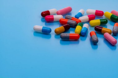 Mavi arka planda renkli kapsül hapları. Reçeteli ilaçlar. Eczacılık. Sağlık ve ilaç servisi. Sağlık bütçesi ve sağlık politikası. Boşluğu olan bir sürü hap. İlaç endüstrisi..