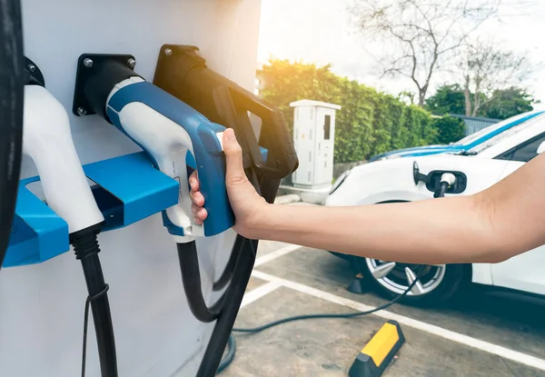 Hand holding electric plug-in charger on blur car charging. EV car charging at electric car charging station. EV car charging point. Electric vehicle fast charge. Sustainable power. Green energy.