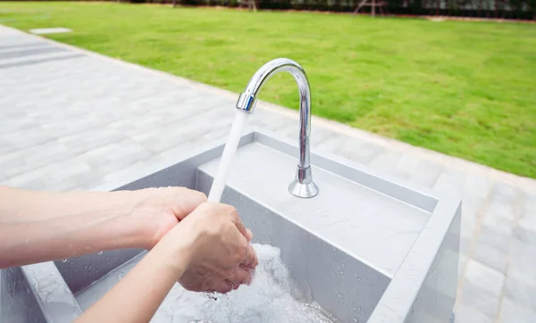 Woman washing hands with tap water under faucet at white sink. Washing hands with tap water at outdoor sink near grass field. Personal hygiene to prevent coronavirus or covid 19. Healthy lifestyle.