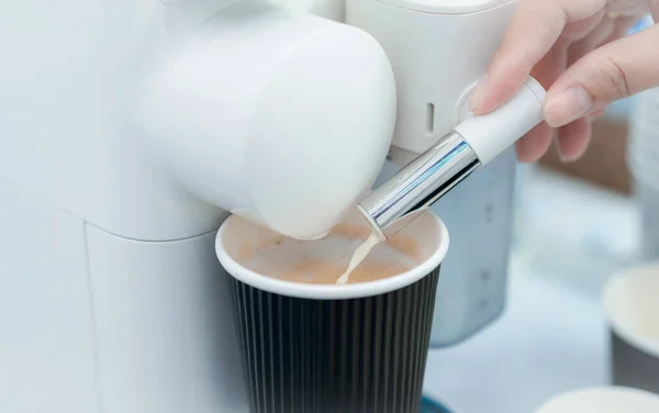 Woman making a cup of hot coffee with capsule coffee machine. Woman hand holding frothed milk dispenser of capsule coffee machine on table. Latte coffee maker. Morning drink. Modern home equipment.