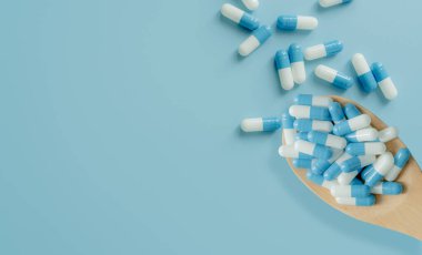 Top view of blue-white antibiotic capsule pills on wooden spoon and blue background. Antibiotic drug resistance. Prescription drug. Medical care. Pharmaceutical care. Antimicrobial drug overuse.