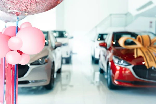 Pink balloons on blur car parked in luxury showroom. New car parked in modern showroom. Car dealership office. Automobile leasing and insurance concept. Auto leasing business. Electric vehicle dealer.