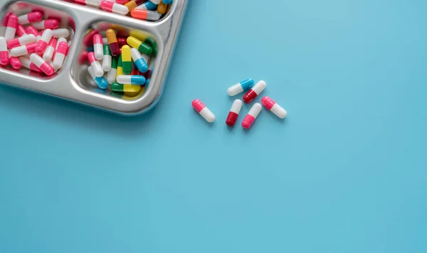 High-angle view of multi-colored antibiotic capsule pills on stainless steel tray and blue background. Antibiotic drug resistance. Prescription drugs. Pharmaceutical industry. Healthcare and medicine.