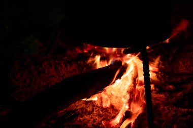 Geceleri şenlik ateşinde yemek pişirmek. Kamp ateşinde aşçı için yakılacak odun yakıtı. Koyu arkaplanda turuncu alevli ateş. Isıtma enerjisi için odun yakıyorum. Kampta akşam yemeği. Kampta ısınmak için ateş..