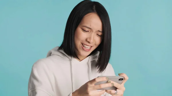 Aasialainen Nainen Näyttää Hermostuneelta Emotionaalisesti Pelaa Älypuhelimella Sinisellä Taustalla Naispelaaja — kuvapankkivalokuva