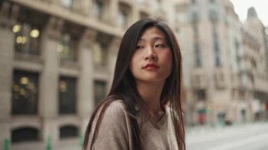 Arka planda geçen arabalarla caddede duran uzun saçlı güzel bir Asyalı kadın. Asyalı kız tek başına şehir merkezine gidiyor.