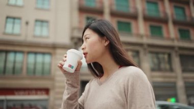 Uzun saçlı Asyalı bir kadının açık havada kahve içerken fotoğrafını çekiyorum. Sıradan giyinmiş güzel bir kız elinde kahveyle şehir merkezine gidiyor. Şehir hayatı konsepti