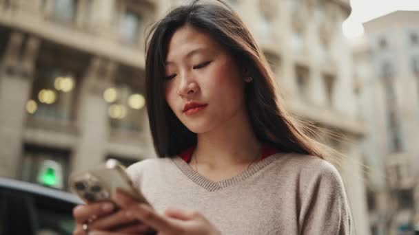 아름다운 아시아인긴 길거리에서 스마트폰으로 친구와 진심으로 웃으며 메시지를 보내는 — 비디오