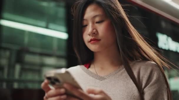 아름다운 아시아인긴 머리를 정류장에서 스마트폰을 사용하여 올바른 목적지를 있었다 — 비디오