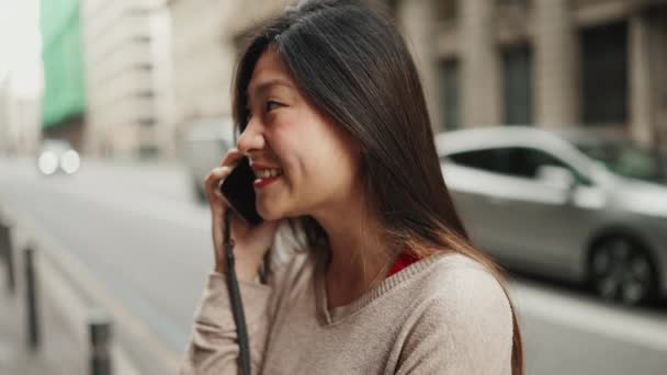 머리의 아시아 스마트폰으로 친구와 소식을 이야기하고 거리에서 미소짓는 — 비디오
