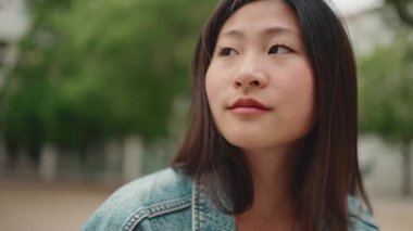 Uzun saçlı Asyalı kadın, kablosuz kulaklık takıyor ve sokakta müzik dinliyor. Çekici kız dışarıda dinleniyor.