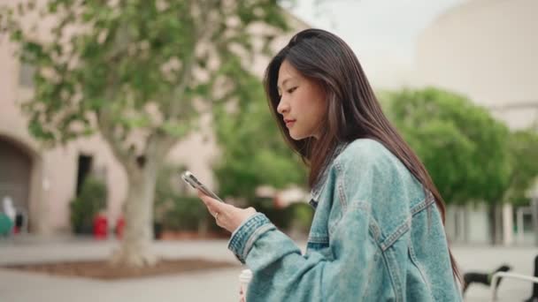 재킷을 거리에서 친구를 기다리는 미디어를 확인하는 아름답고 아시아 소녀의 — 비디오