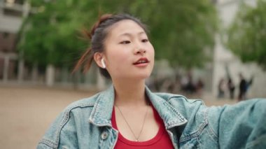 Kablosuz kulaklık takan çekici Asyalı kız dışarıda akıllı telefon kullanarak sosyal medyası için video çekiyor. İçerik oluşturan kadın blog yazarı