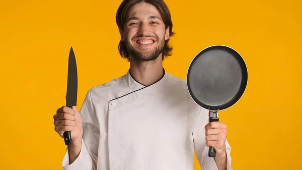 유니폼을 프라이팬을 긍정적 요리사가 노란색 카메라에서 즐거움을 기구를 준비가 젊은이 — 스톡 사진