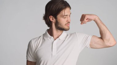Beden eğitiminden sonra pazılarını gösteren çekici sakallı bir adam gri arka planda kendine güveniyor. Sportif adam vücut gücünü gösteriyor.
