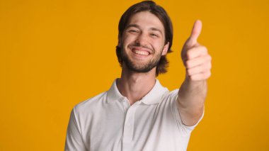 Pozitif esmer adam sarı arka planda parmağını yukarıda tutuyor. Çekici adam kameraya gülümsüyor.
