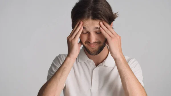 Young thoughtful man looking tired keeping hands on head over gray background. Man looking confused forgot to do work isolated