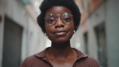 Gözlüklü güzel Afrikalı kadının dışarıda mutlu olduğu yakın plan çekimler. Şehir caddesinde kameraya bakıp gülümseyen koyu tenli bir kız. Yüz ifadesi kavramı