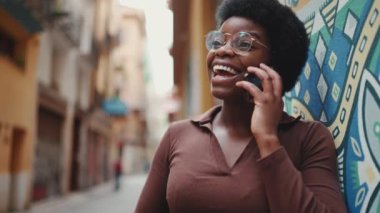 Akıllı telefondan konuşan çekici Afrikalı kız dışarıda mutlu görünüyor. Neşeli kadın sokakta cep telefonunu kullanarak arkadaşıyla konuşuyor.