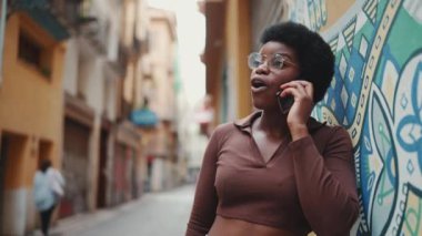 Açık havada akıllı telefondan konuşan çekici Afrikalı kız. Neşeli kadın sokakta cep telefonu kullanarak arkadaşıyla konuşuyor.